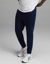 A person wearing a white shirt, Cozy Earth Men’s Recovery Jogger in navy, and white athletic sneakers stands against a plain gray background.|Color:Navy