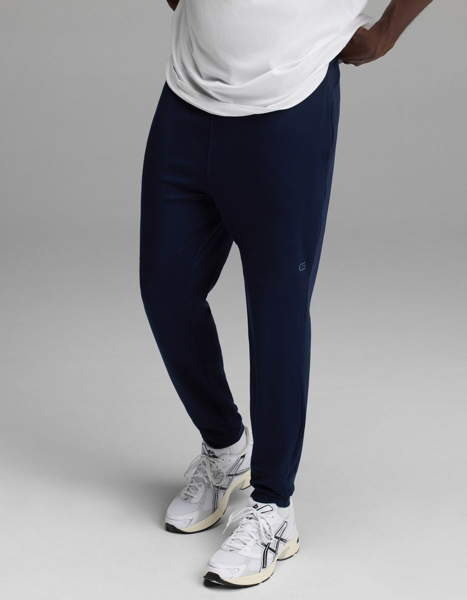 A person wearing a white shirt, Cozy Earth Men’s Recovery Jogger in navy, and white athletic sneakers stands against a plain gray background.|Color:Navy