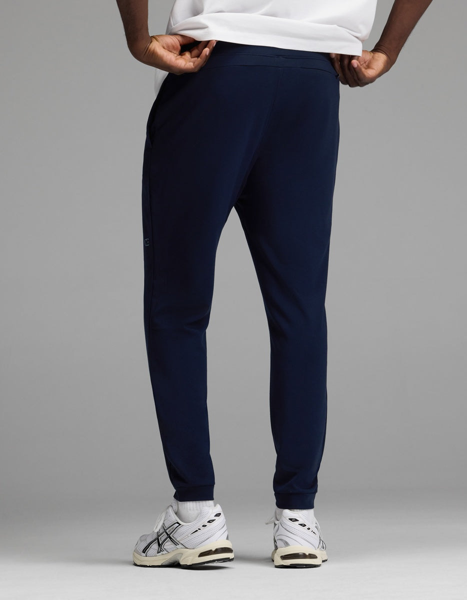 A man models the Cozy Earth Men’s Recovery Jogger in navy, paired with white sneakers featuring black accents and a white shirt, standing against a plain gray backdrop. The photo highlights the back view of the lower body.|Color:Navy