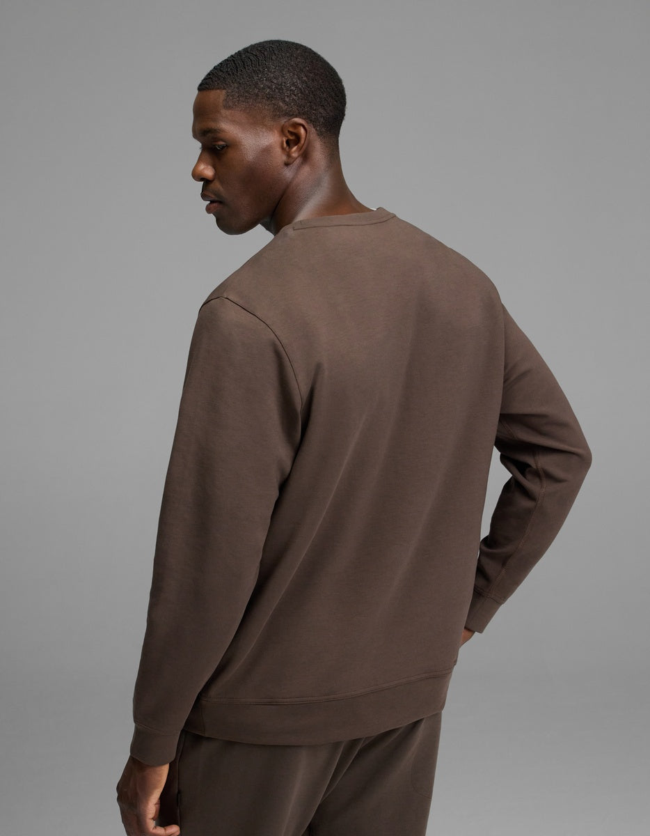 A man stands facing away, wearing the Cozy Earth Men’s StretchTech Crewneck and matching pants against a plain gray background.