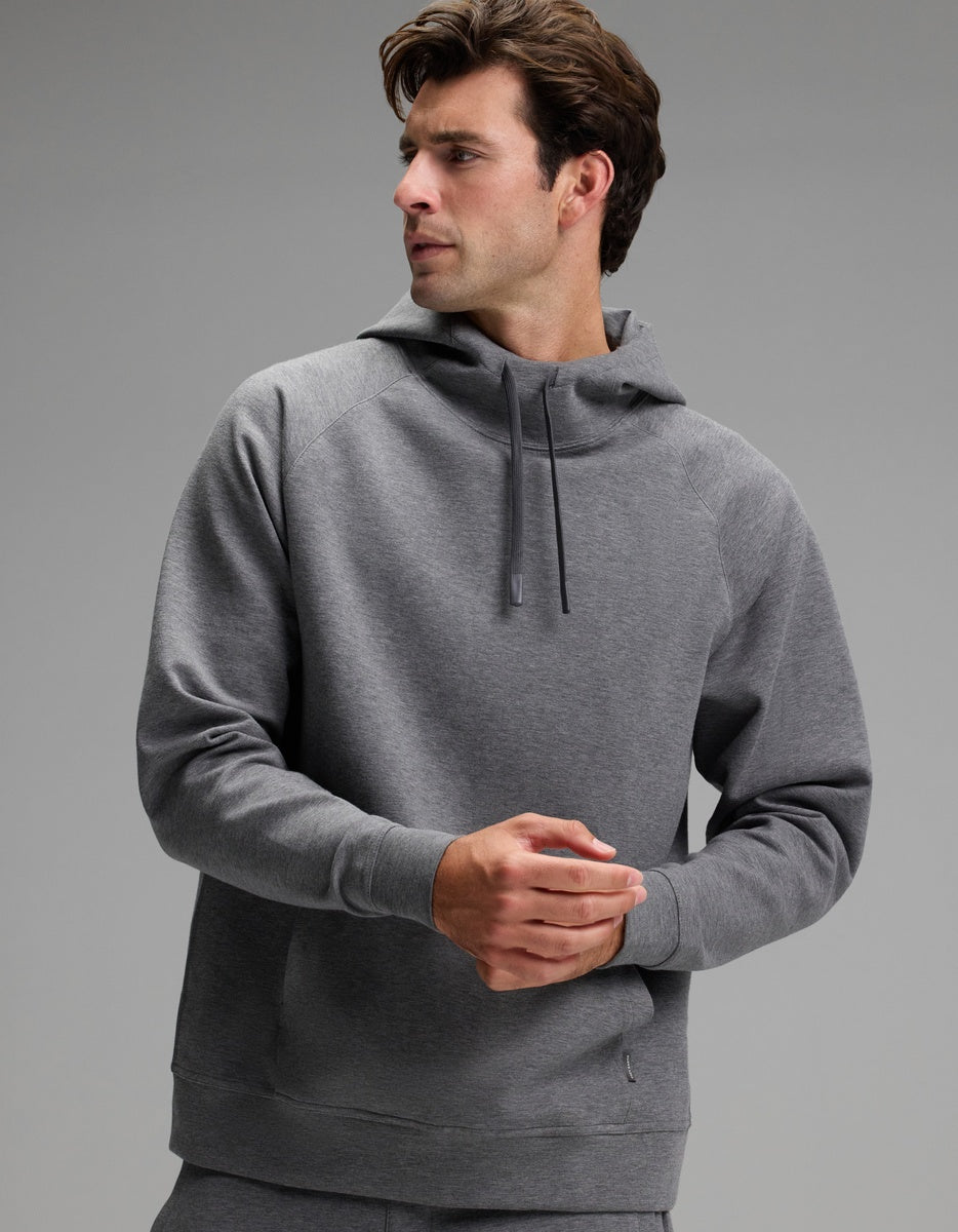 A man wearing the Cozy Earth Men’s StretchTech Hoodie in gray stands against a plain gray background, looking to his left with his hands clasped.|Color:Coal Heather