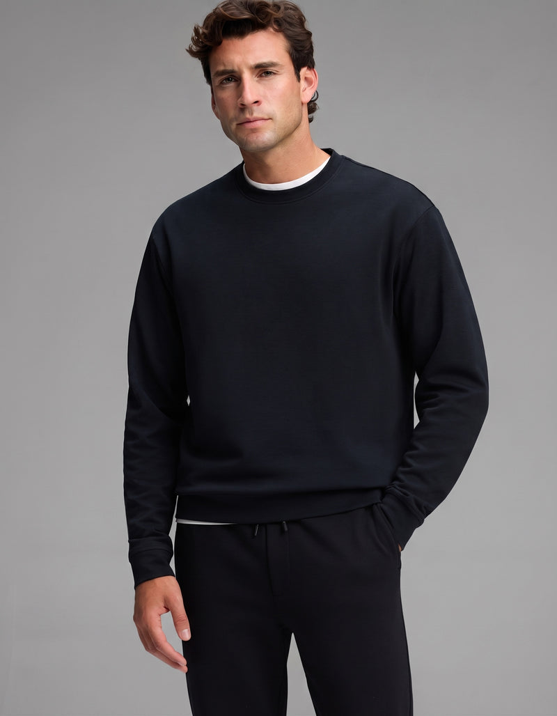 A man with short brown hair wears the Cozy Earth Men's Versa Crewneck & Jogger Set in black over a white shirt, standing against a plain gray background and looking at the camera with a neutral expression.