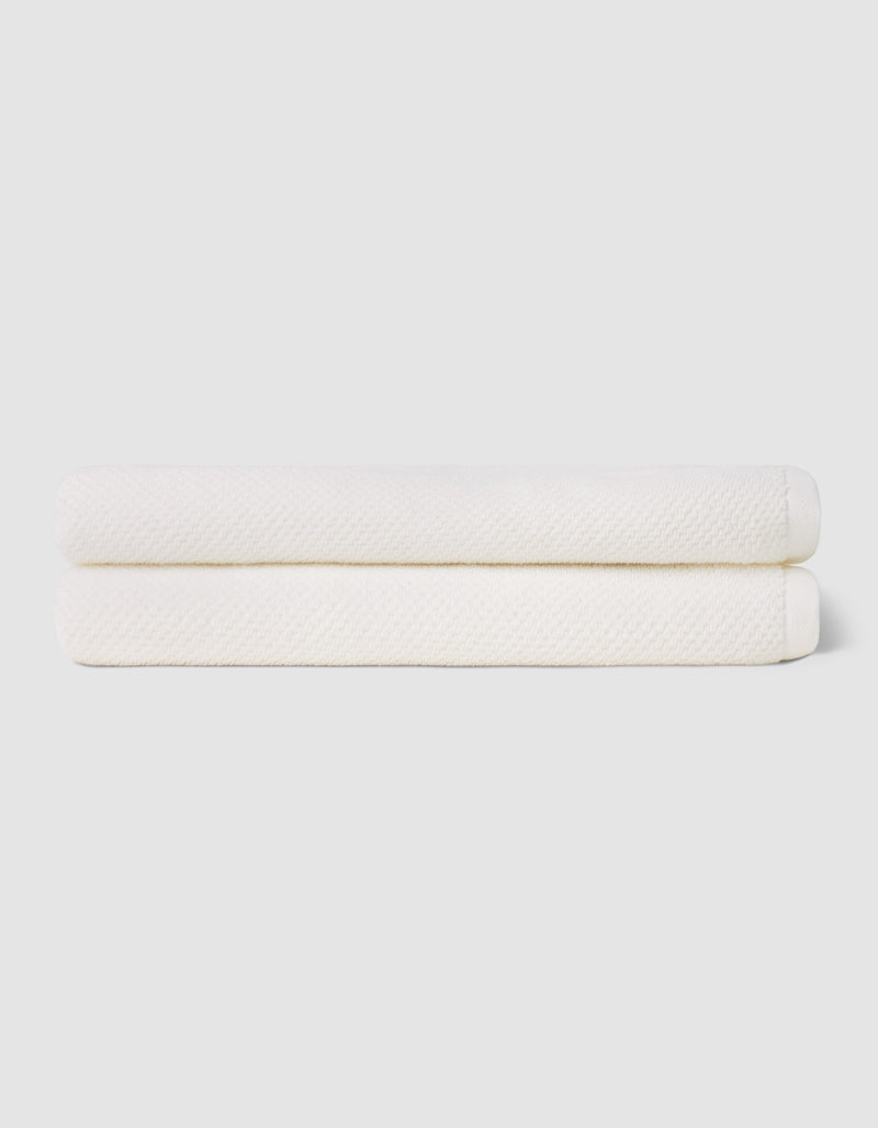 Two neatly folded Cozy Earth Nantucket Bath Sheets are stacked atop each other against a plain, light-colored background.