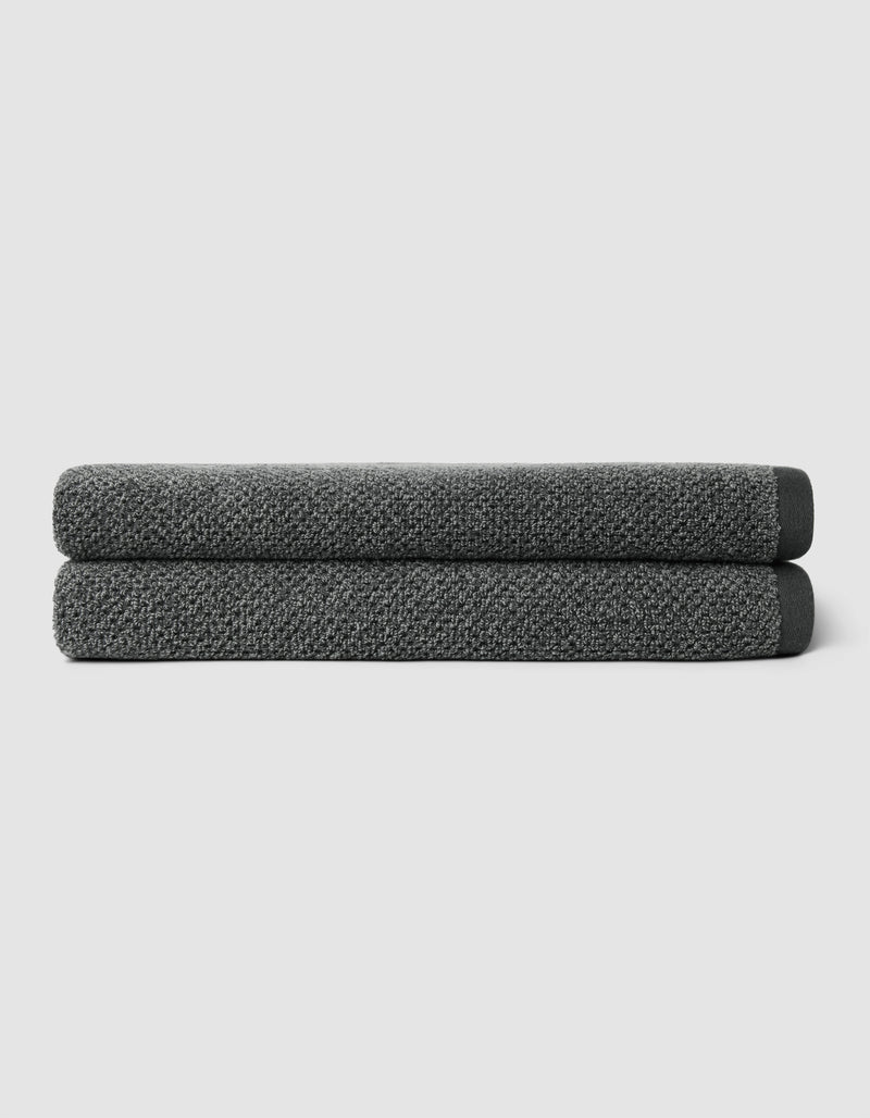 Two neatly folded Nantucket Bath Towels by Cozy Earth, in dark gray, are stacked atop one another against a plain light gray background.