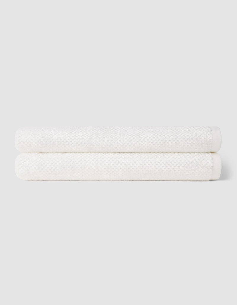 Two neatly folded Nantucket Bath Towels by Cozy Earth are stacked together against a plain light gray background.