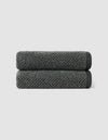Two dark gray Nantucket Hand Towels by Cozy Earth, neatly rolled and stacked, set against a plain light gray background.|Color:Graphite