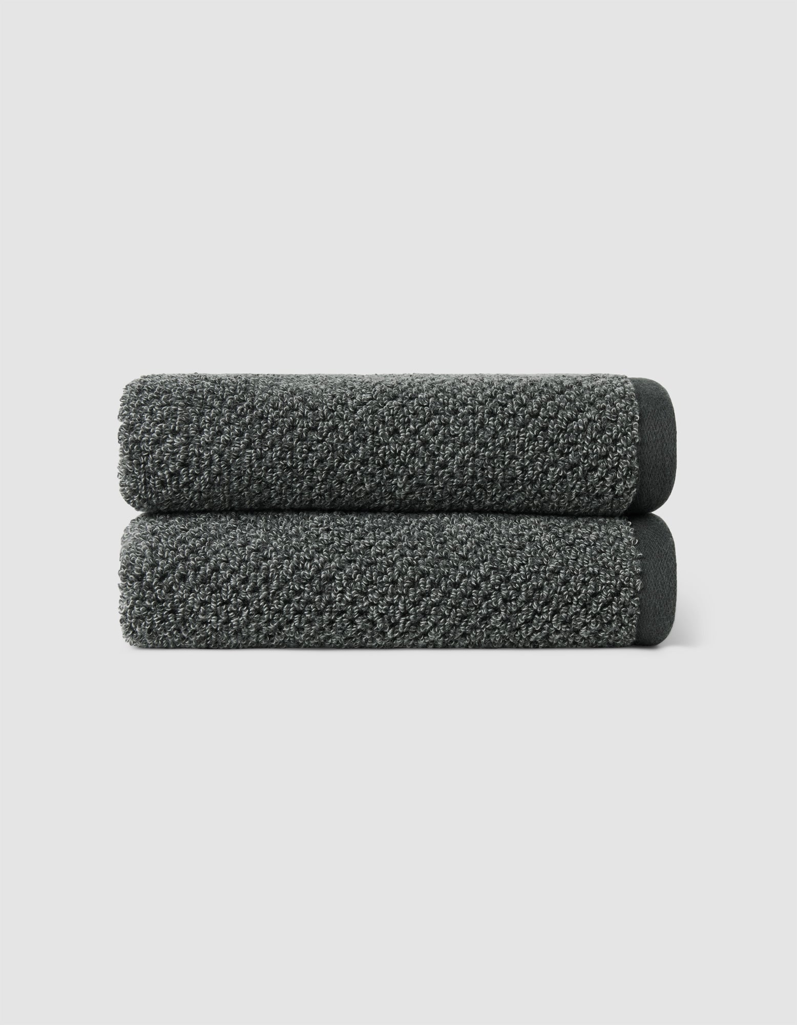 Two dark gray Nantucket Hand Towels by Cozy Earth, neatly rolled and stacked, set against a plain light gray background.|Color:Graphite