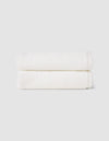 Two Nantucket Hand Towels by Cozy Earth, neatly folded and stacked, are displayed against a plain light gray background.|Color:White