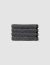 Four neatly folded Nantucket Washcloths by Cozy Earth, textured in dark gray, are stacked horizontally on a plain light gray background.|Color:Graphite