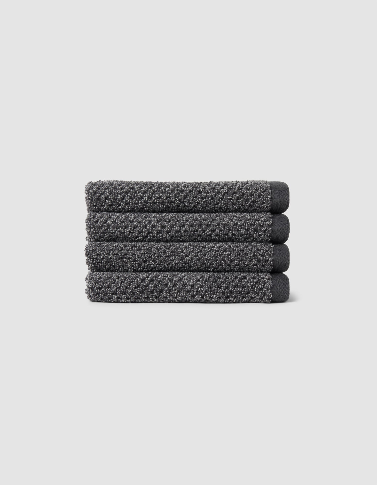 Four neatly folded Nantucket Washcloths by Cozy Earth, textured in dark gray, are stacked horizontally on a plain light gray background.|Color:Graphite
