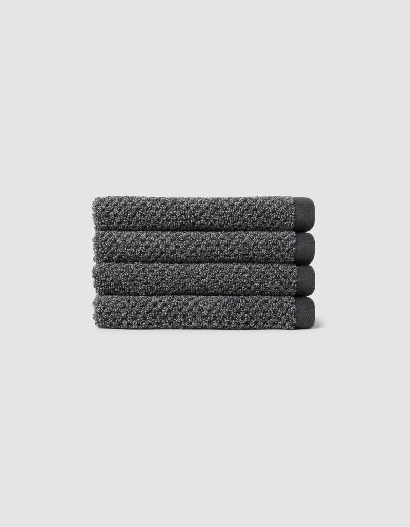Four neatly folded Nantucket Washcloths by Cozy Earth, textured in dark gray, are stacked horizontally on a plain light gray background.