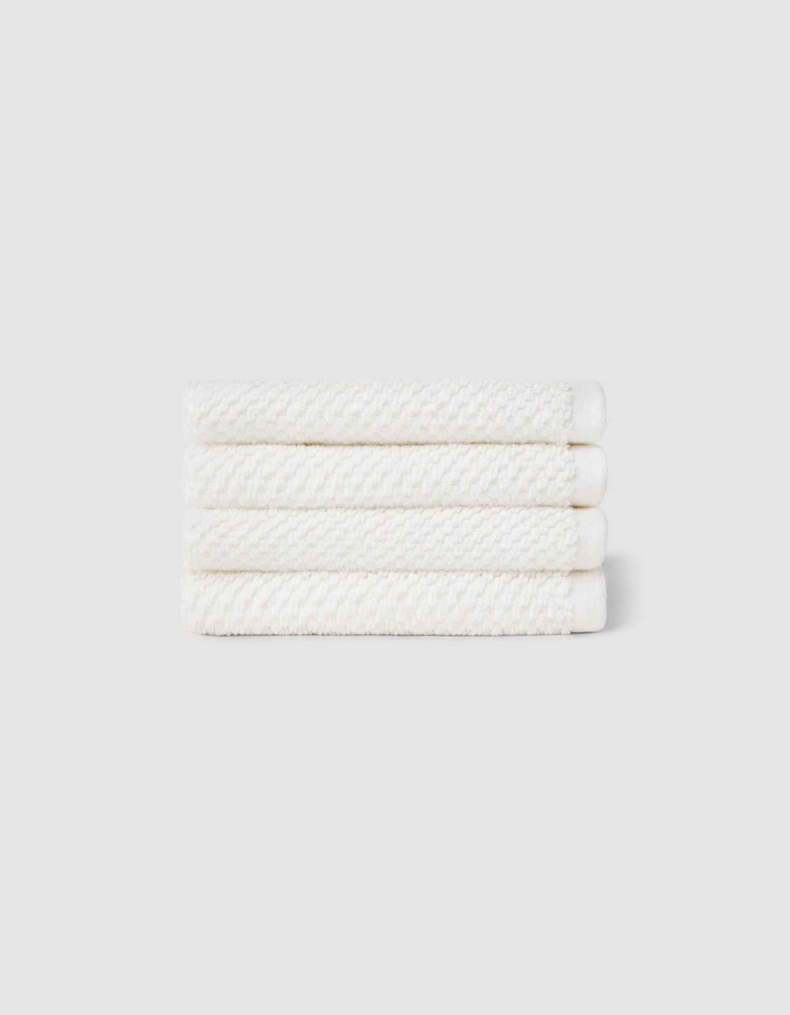 Four neatly folded Nantucket Washcloths by Cozy Earth, stacked horizontally against a plain light gray background.|Color:White