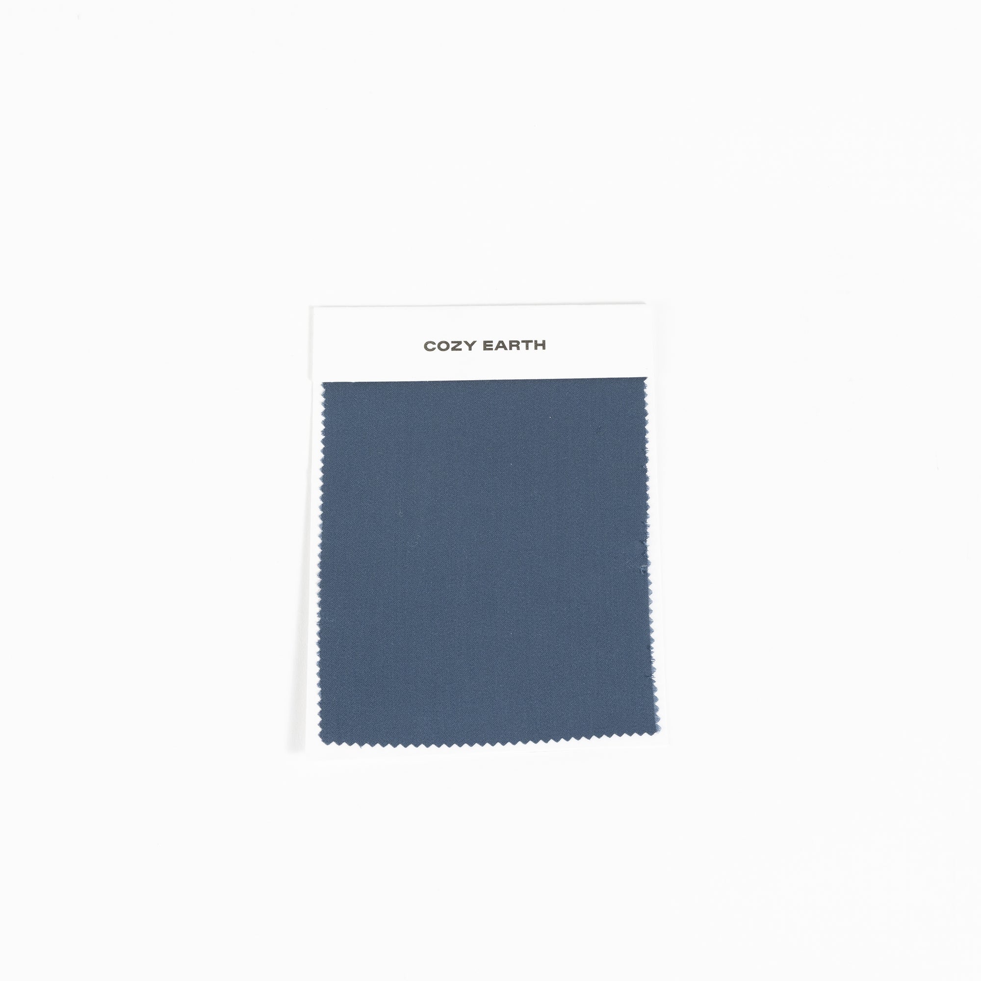 A fabric swatch from the Bamboo Sheet collection by Cozy Earth features a deep blue color, with zigzag-cut edges, set against a plain white background. 