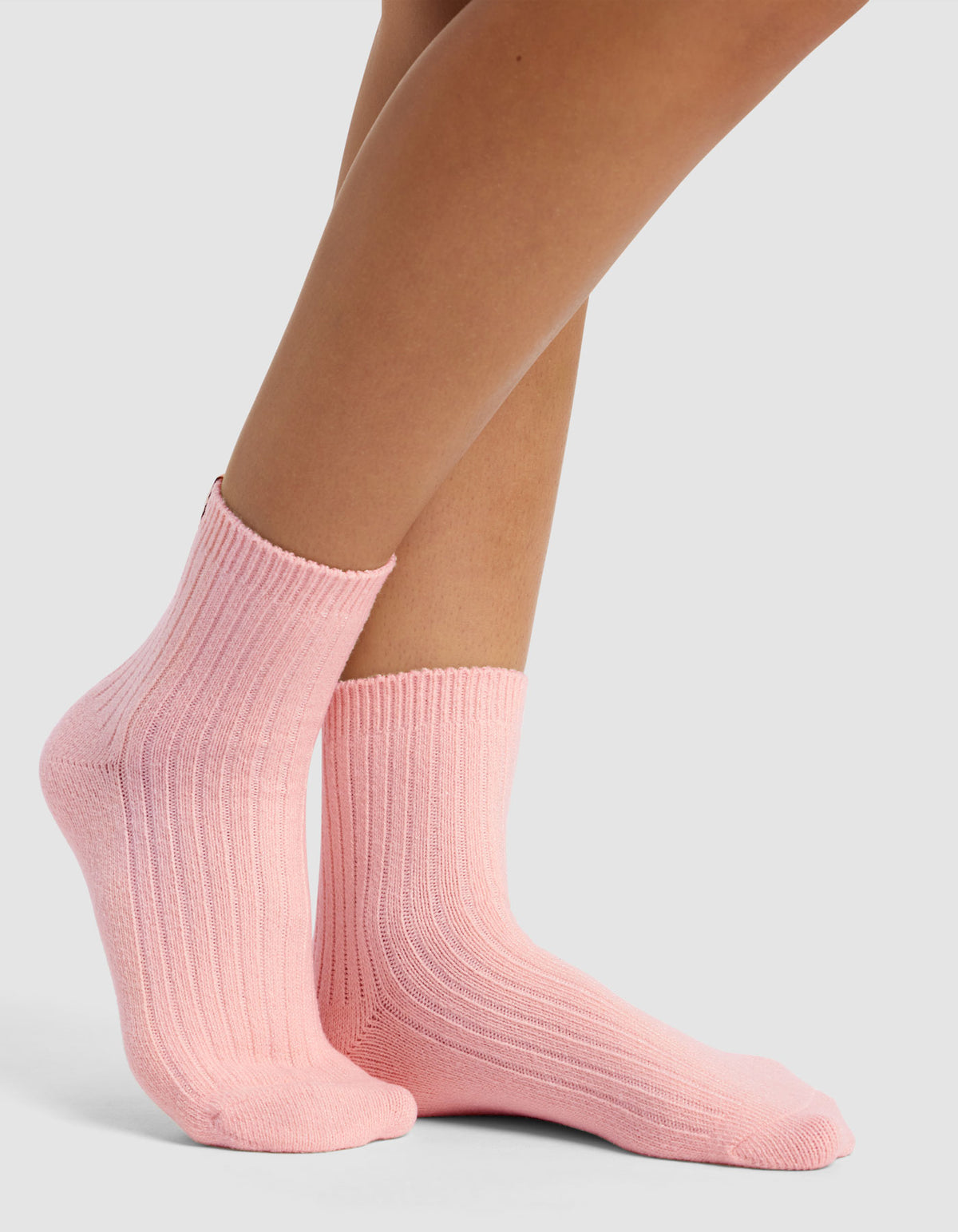 A pair of feet wears The Plush Modern Crew Sock by Cozy Earth in light pink, featuring a ribbed, cozy texture against a plain light gray background.|Color:Tulip