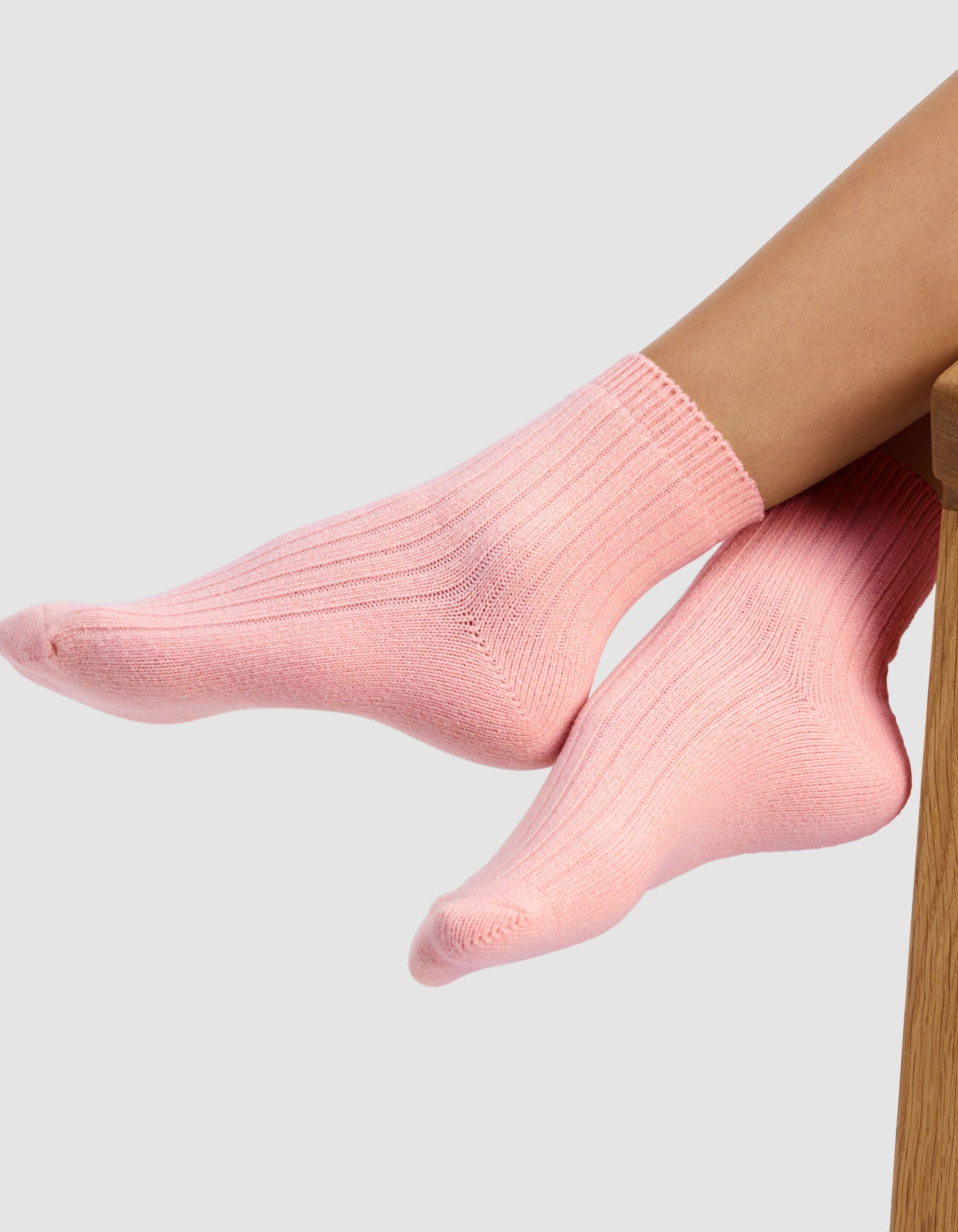 Someone wearing Cozy Earth’s Plush Lounge Quarter Socks (light pink, from the 3-Pack) rests their feet on wood with a plain light gray backdrop.