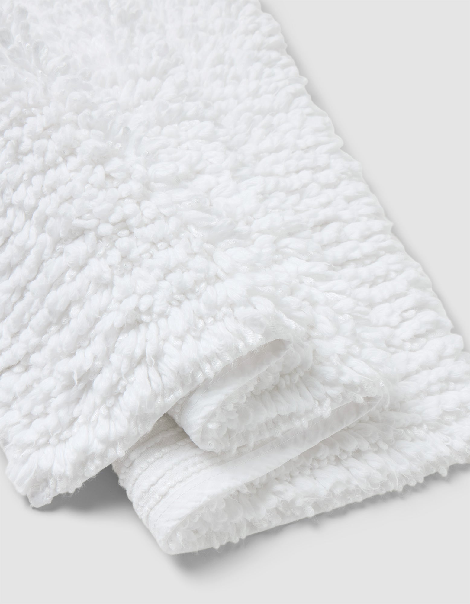A close-up of the Cozy Earth Plush Loop Bath Mat, folded on a light gray background. The mat’s fluffy, looped texture highlights its softness and absorbency.|Color:White