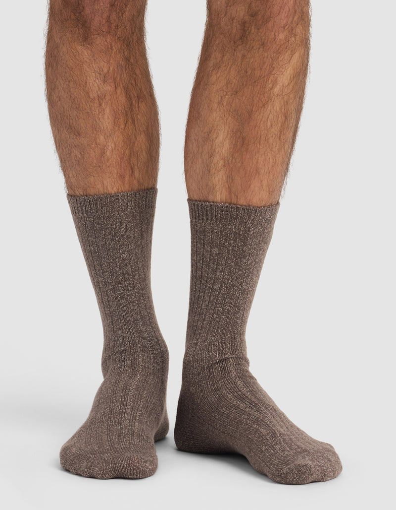 A close-up of a person's lower legs and feet wearing Cozy Earth’s The Plush Lounge Calf Sock 3-Pack in brown, ribbed, crew-length style, set against a plain white background.