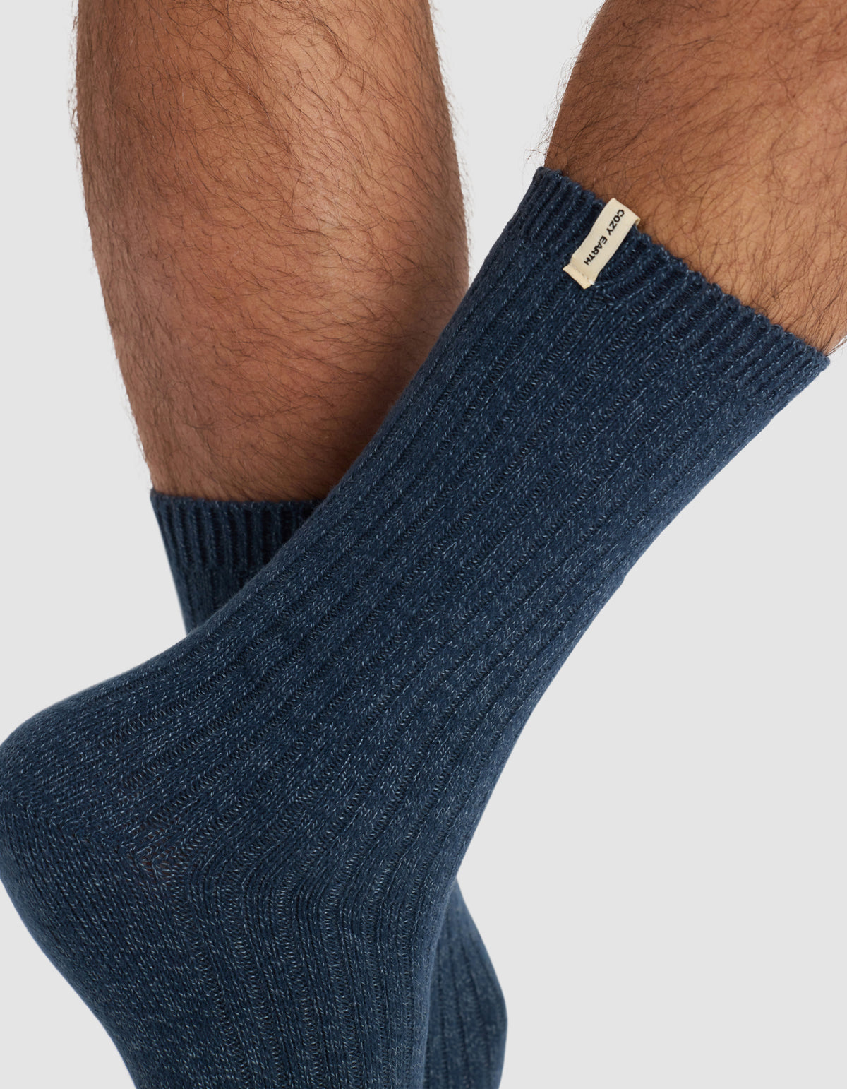 Close-up of a person’s lower legs wearing Cozy Earth's The Plush Lounge Calf Sock 3-Pack in ribbed dark blue, featuring a small beige label near the top, set against a plain light background.