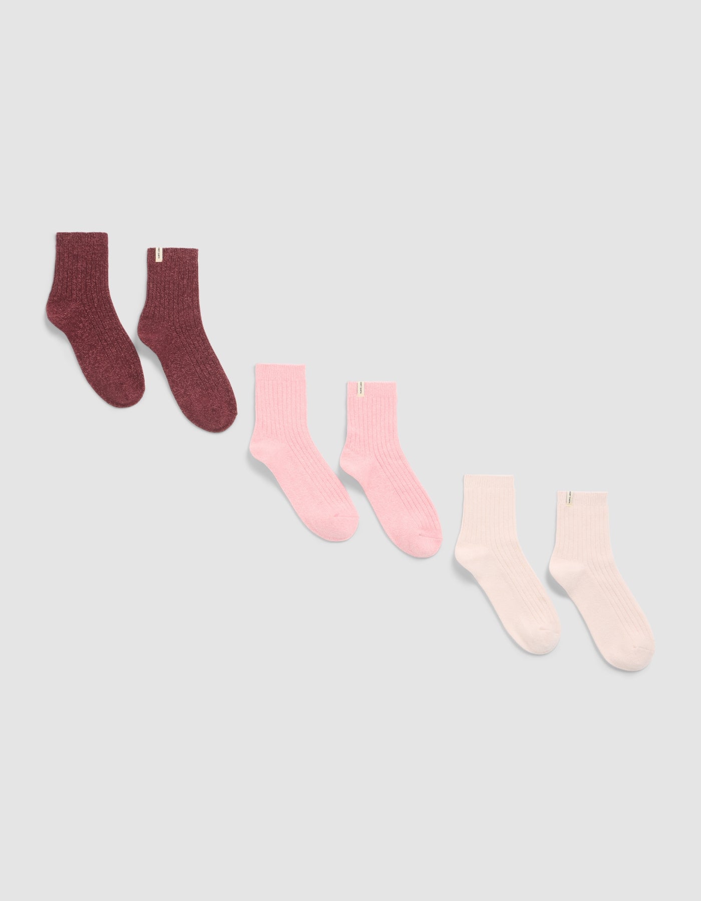 Three pairs of The Plush Lounge Quarter Sock 3-Pack by Cozy Earth, displayed diagonally on a light background in dark burgundy, pink, and light pink or white shades.|Color:Burgundy/Tulip/Blossom