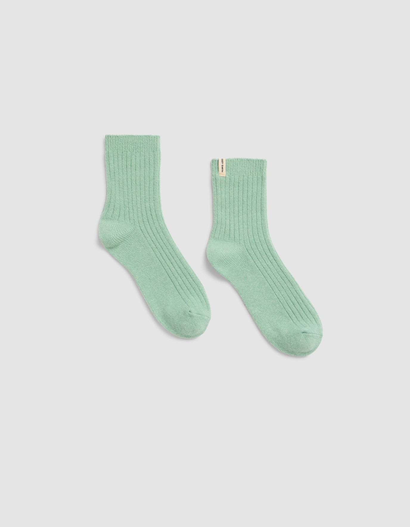 A pair of Plush Lounge Quarter Sock by Cozy Earth, in light green ribbed fabric, is laid flat on a plain white background with one sock slightly angled outward.