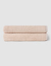 The Complete Ribbed Terry Bath Bundle by Cozy Earth features two neatly rolled, light beige towels stacked on a plain, light gray background.|Color:Petal