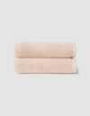 The Cozy Earth Complete Ribbed Terry Bath Bundle features two neatly folded, light beige towels stacked atop each other against a plain, light gray background.|Color:Petal
