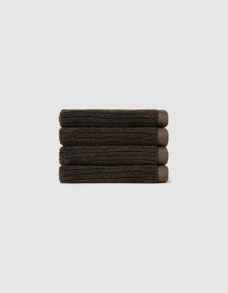 The Cozy Earth Complete Ribbed Terry Bath Bundle, featuring four dark brown towels, is arranged horizontally against a plain light gray background.