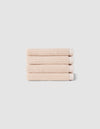 The Complete Ribbed Terry Bath Bundle by Cozy Earth features four neatly folded beige towels stacked atop each other against a plain light gray background.|Color:Petal