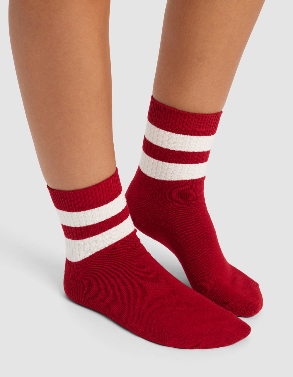 Two feet wearing Cozy Earth's Women's Sadie Sock, featuring red crew style with two white ankle stripes, shown against a light gray background.|Color:Crimson/Bone