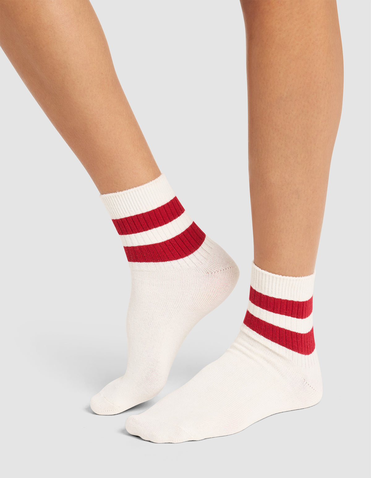 Two legs wearing Cozy Earth's Women's Sadie Sock—white ribbed socks with two thick red stripes at the ankles—stand on a light grey background.  |Color:Bone/Crimson