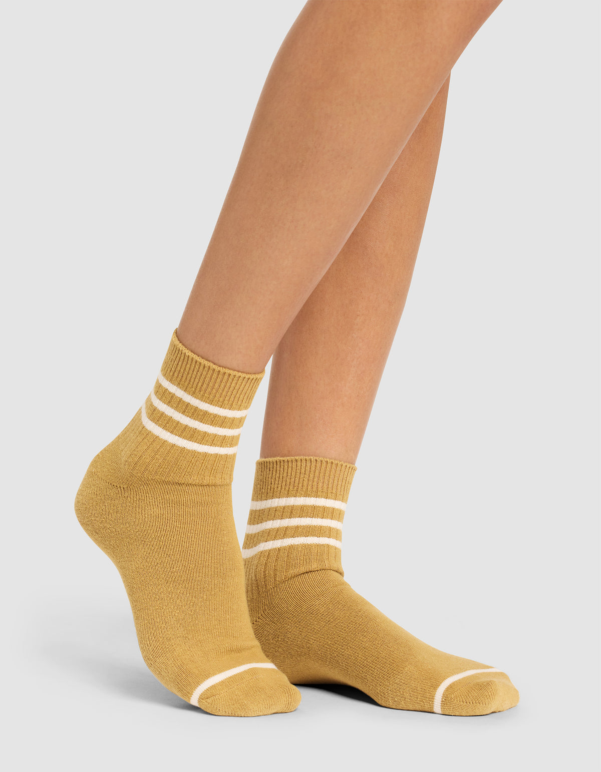A person wears Cozy Earth Women's Sadie Socks in mustard yellow with white stripes at the ankle and toes, standing against a plain light background. |Color:Dijon/Alabaster