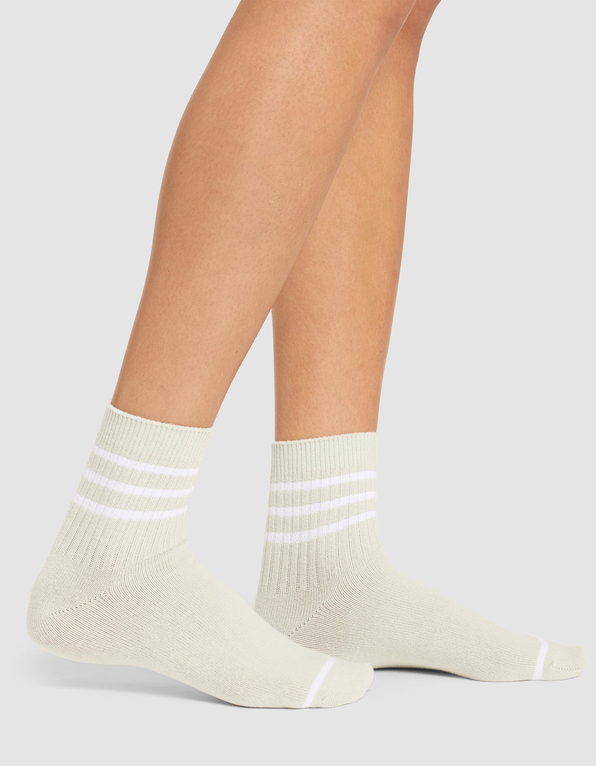 A person is wearing Cozy Earth's Women's Sadie Sock—light-colored ankle socks with three white stripes near the cuffs—while standing on a white background. |Color:Laurel/White