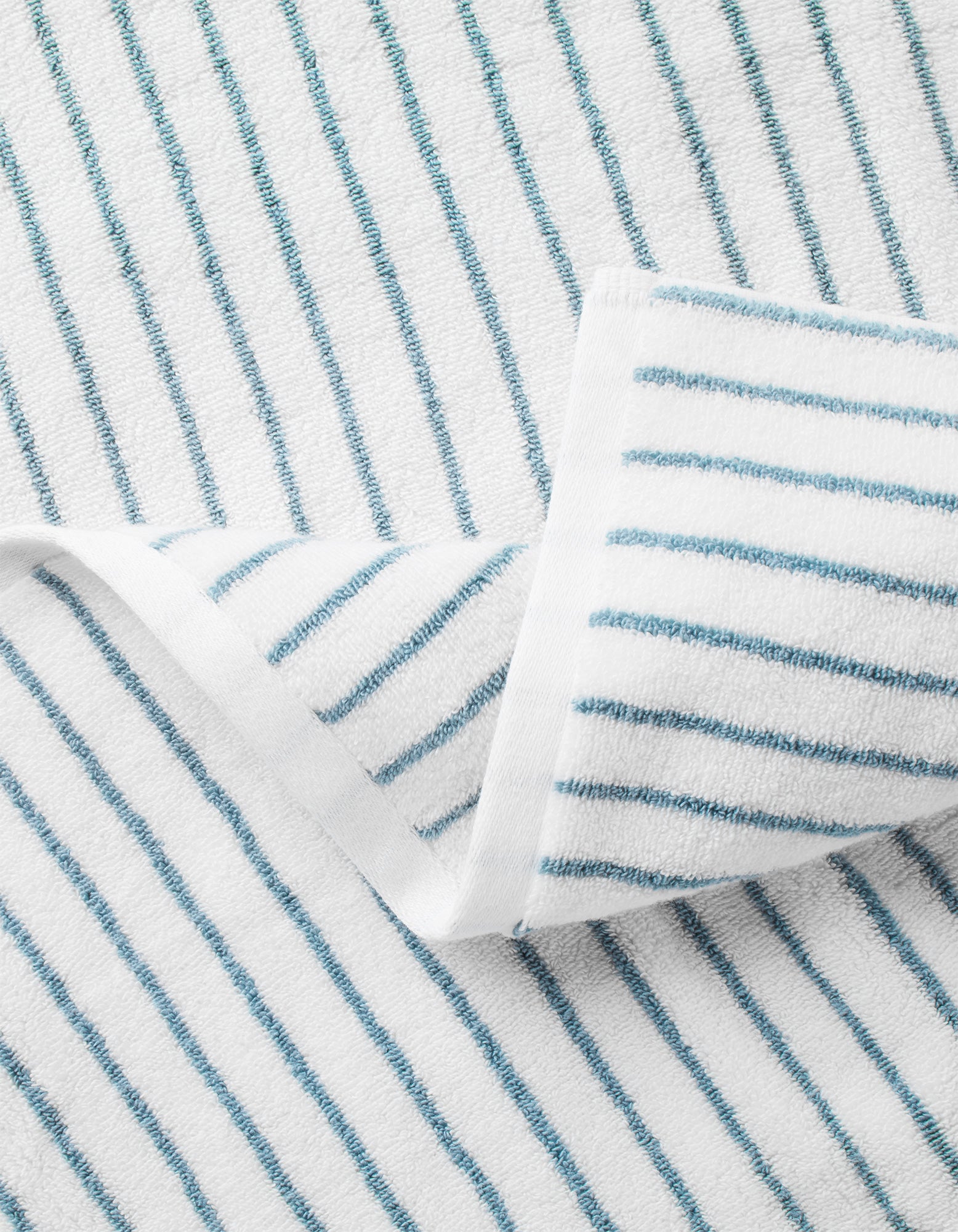 Close-up of Cozy Earth's Striped Luxe Washcloths in white with evenly spaced thin blue stripes and a folded corner, highlighting the fabric's texture and pattern. 