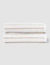 Two Striped Luxe Hand Towels by Cozy Earth, in white with light brown stripes, are neatly folded and stacked against a plain light gray background. |Color:Sand Stripe