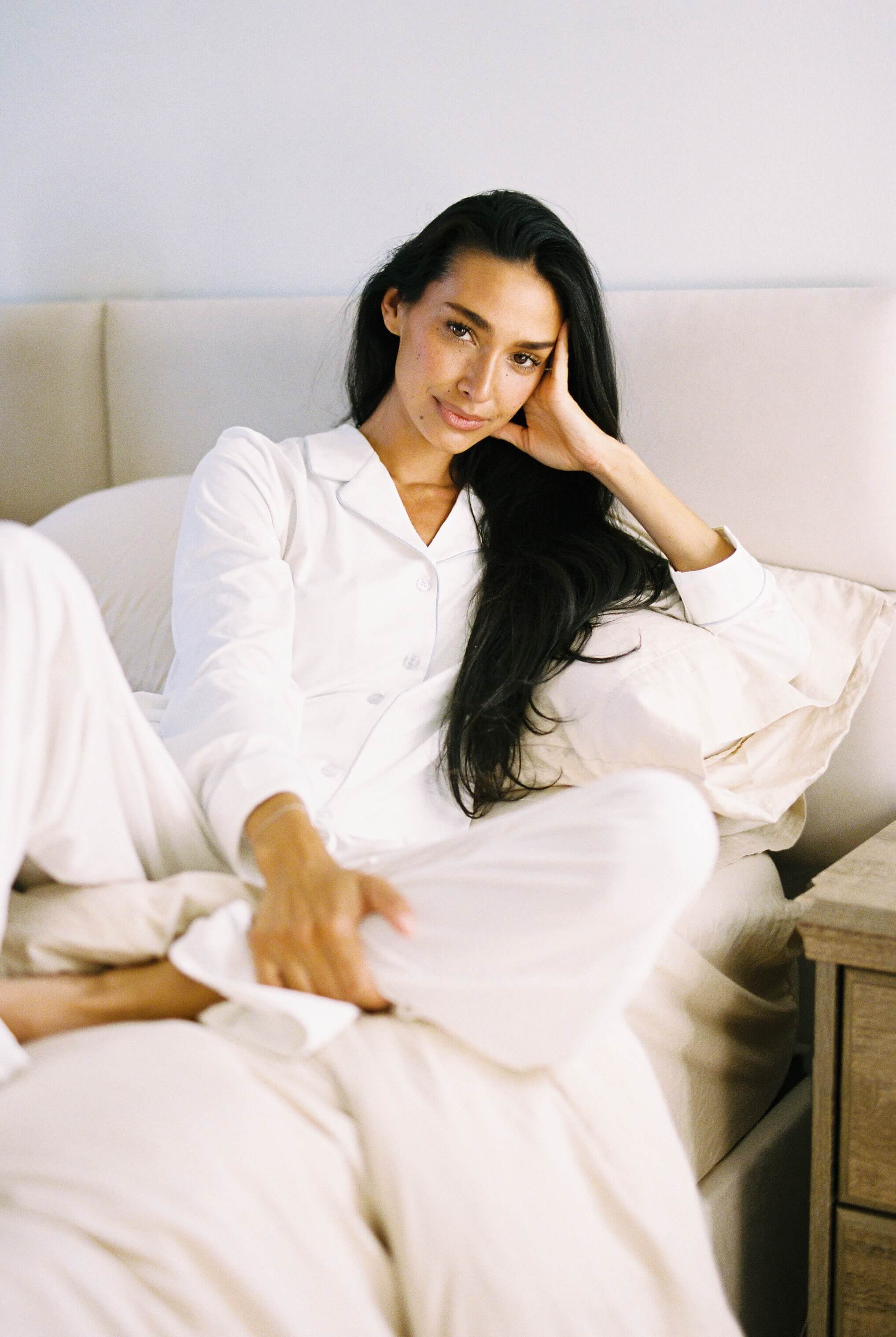 Woman in a white pajama set sitting on a bed in a bright room