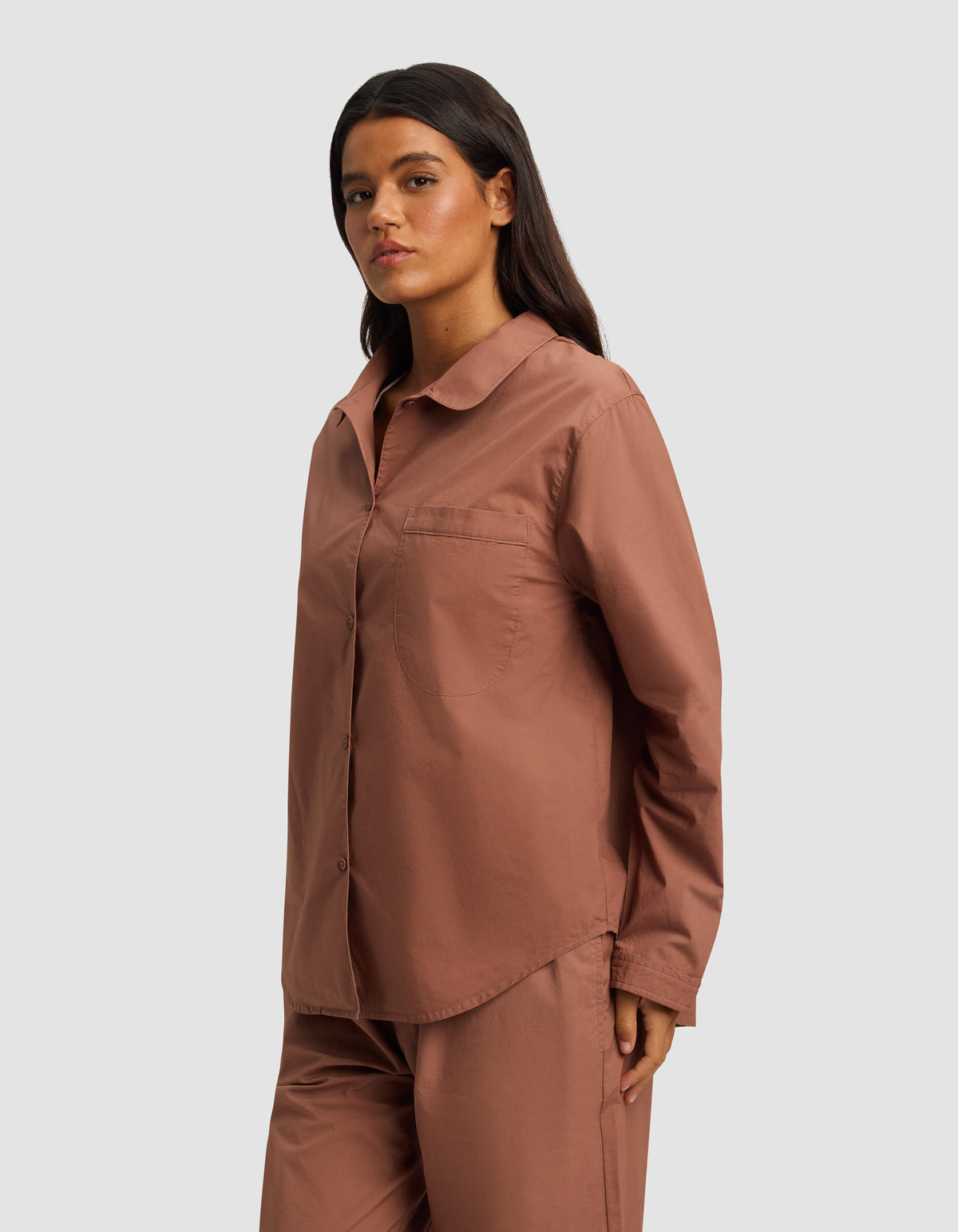 A woman with long dark hair wears the Cozy Earth Women's Sutton Long Sleeve Pajama Top in dusty rose, paired with matching pants, standing against a plain light gray background.|Color:Saddle