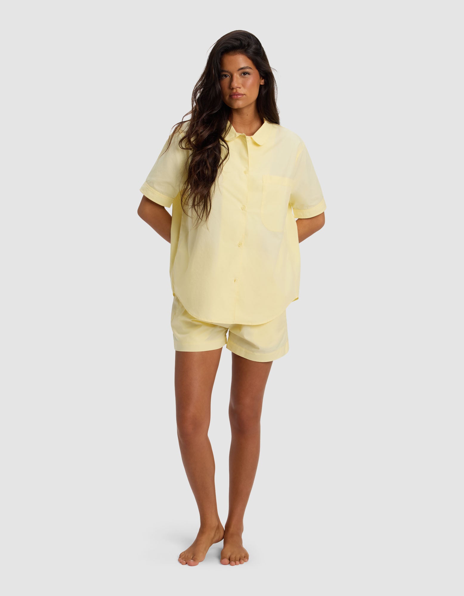 A woman stands barefoot against a plain background, wearing the Cozy Earth Women's Sutton Short Sleeve Pajama Set in light yellow, with her hands in her pockets.|Color:Meringue