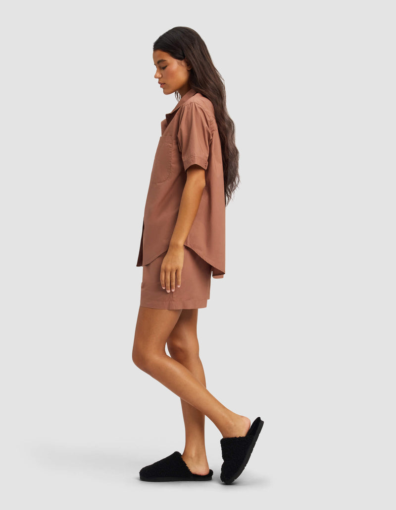 A woman with long dark hair stands in profile, wearing the Cozy Earth Women's Sutton Short Sleeve Pajama Set in brown against a plain light background.