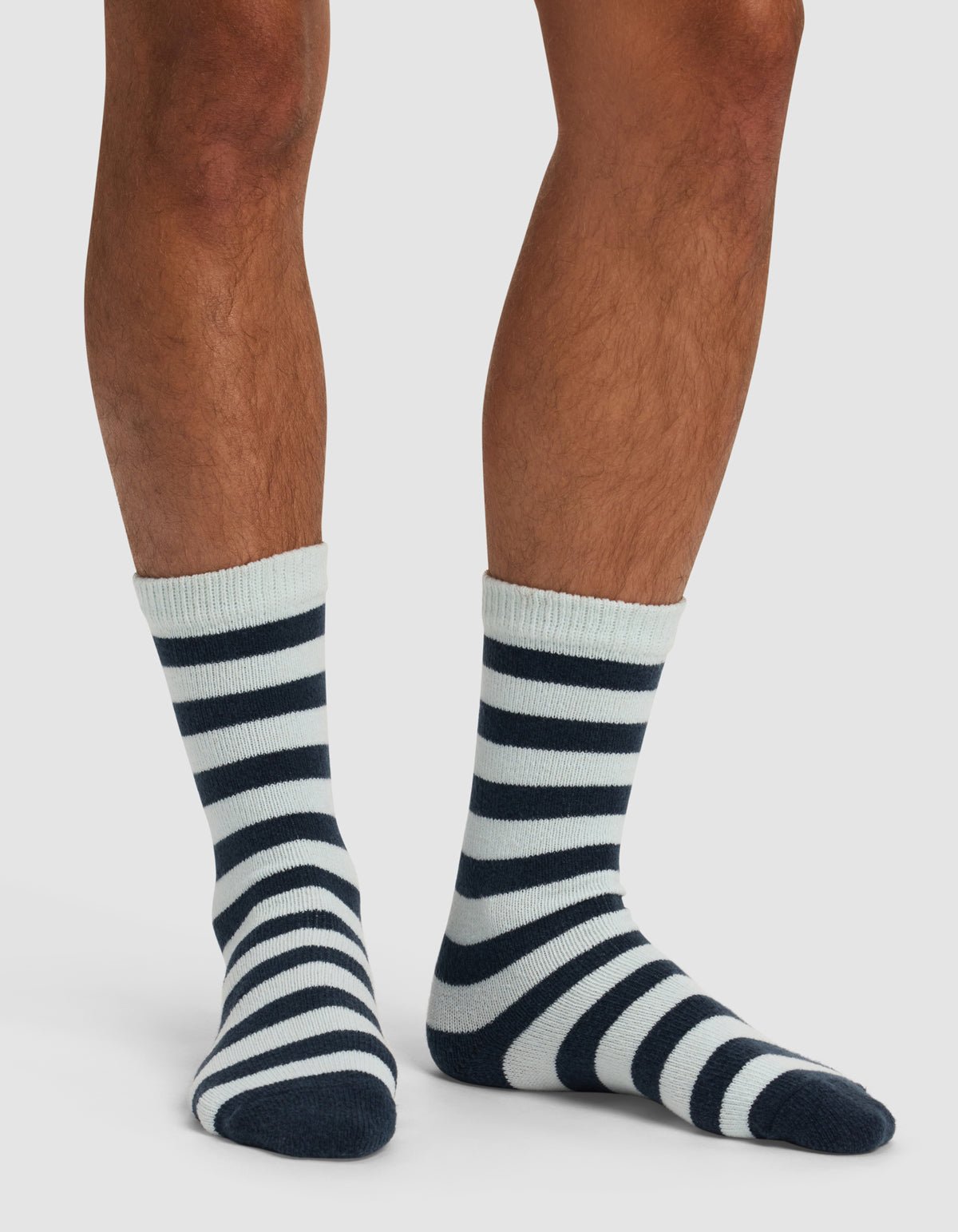 A person showcases only their lower legs and feet in Cozy Earth's The Striped Plush Lounge Sock, featuring black and white stripes, against a plain white background.|Color:Mist Stripe