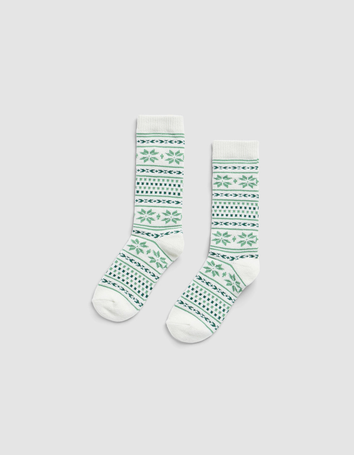 The Snowflake Plush Lounge Sock by Cozy Earth, a pair of white crew socks with green and blue geometric and floral patterns, displayed flat on a plain light gray background.|Color:Celadon