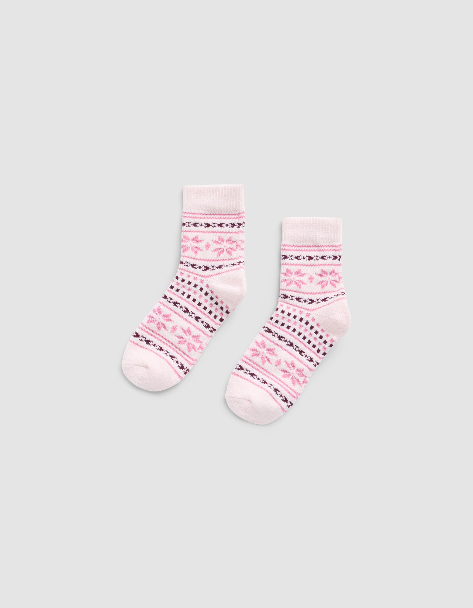 The Snowflake Plush Modern Crew Sock by Cozy Earth is a light pink pair featuring darker pink and black geometric patterns, including stripes and star shapes, displayed flat on a plain gray background.