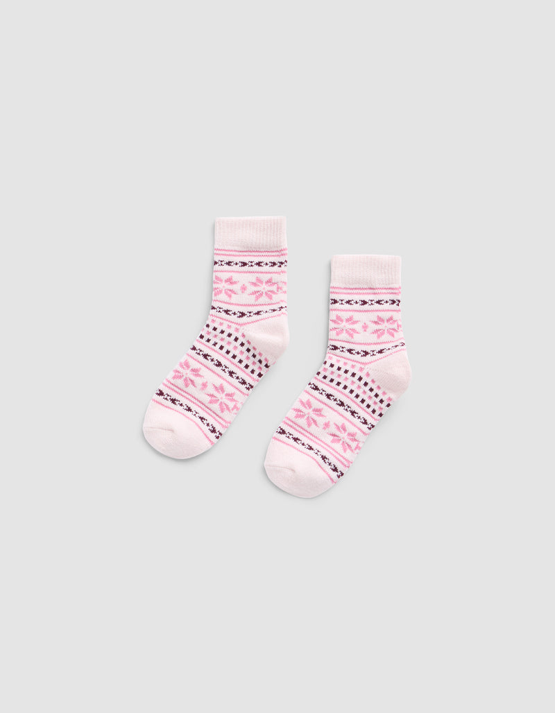 The Snowflake Plush Modern Crew Sock by Cozy Earth is a light pink pair featuring darker pink and black geometric patterns, including stripes and star shapes, displayed flat on a plain gray background.
