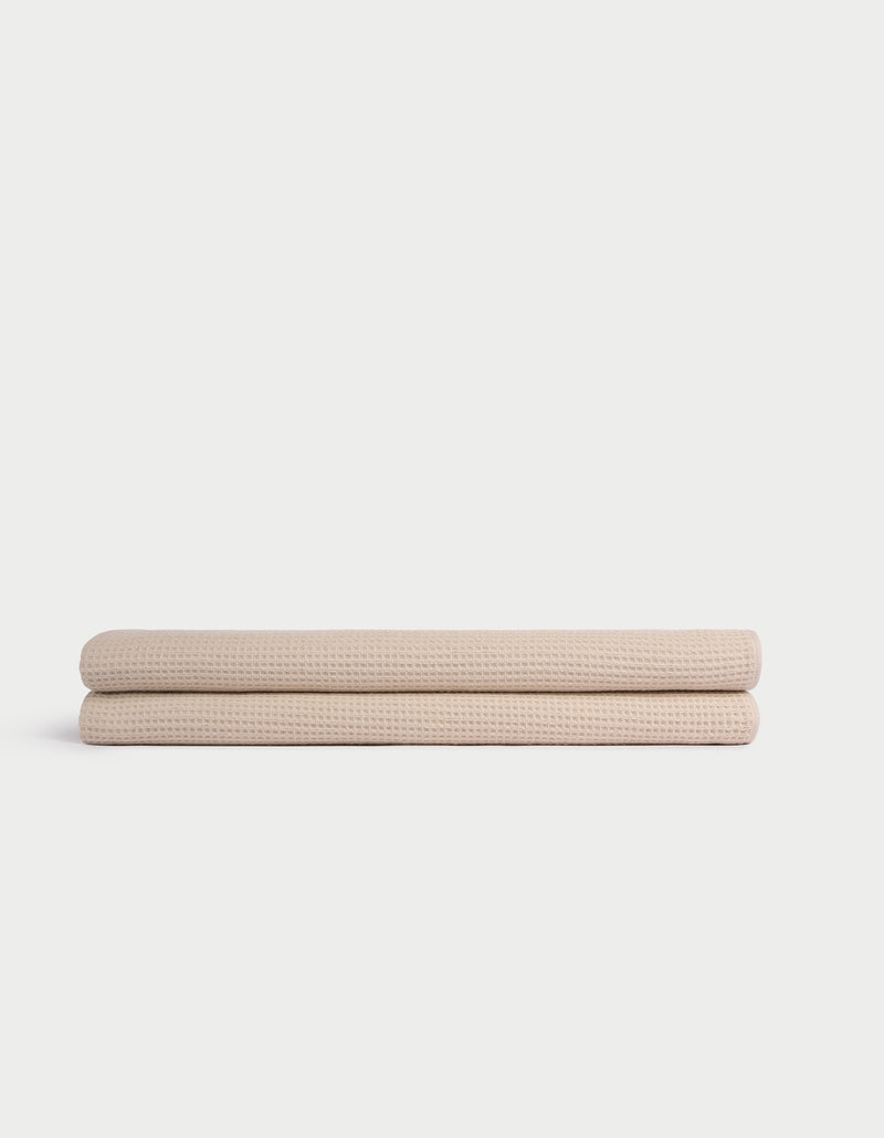 Two Cozy Earth Waffle Bath Sheets, beige and neatly folded, are stacked atop one another against a plain white background.