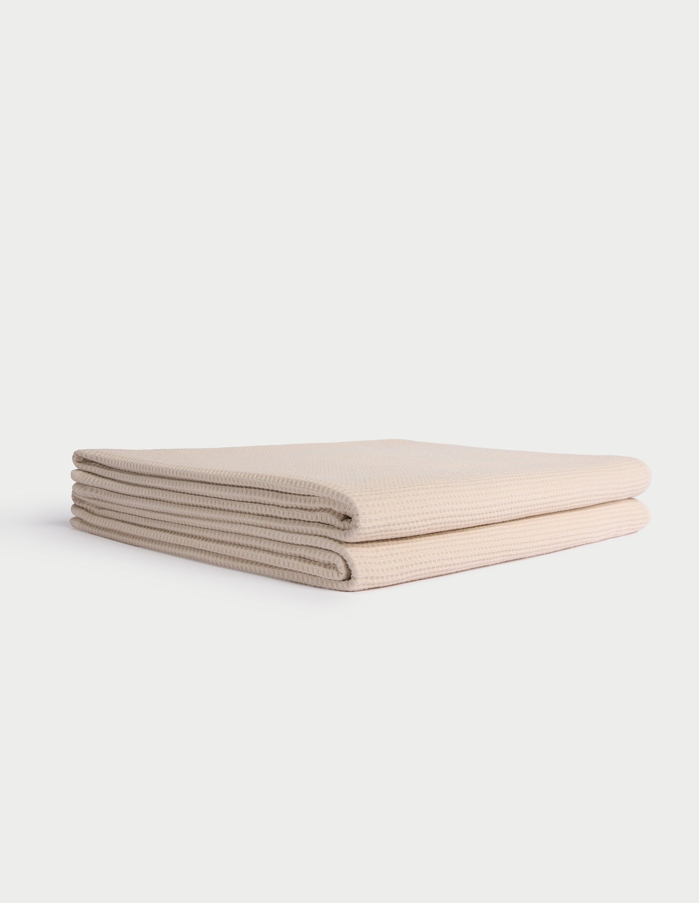 A neatly folded, light beige Cozy Earth Waffle Bath Towel lies on a white background. |Color:Birch
