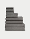 The Complete Waffle Bath Bundle by Cozy Earth features a neatly stacked set of dark gray waffle-textured towels, arranged from largest to smallest, against a plain white background.|Color:Charcoal