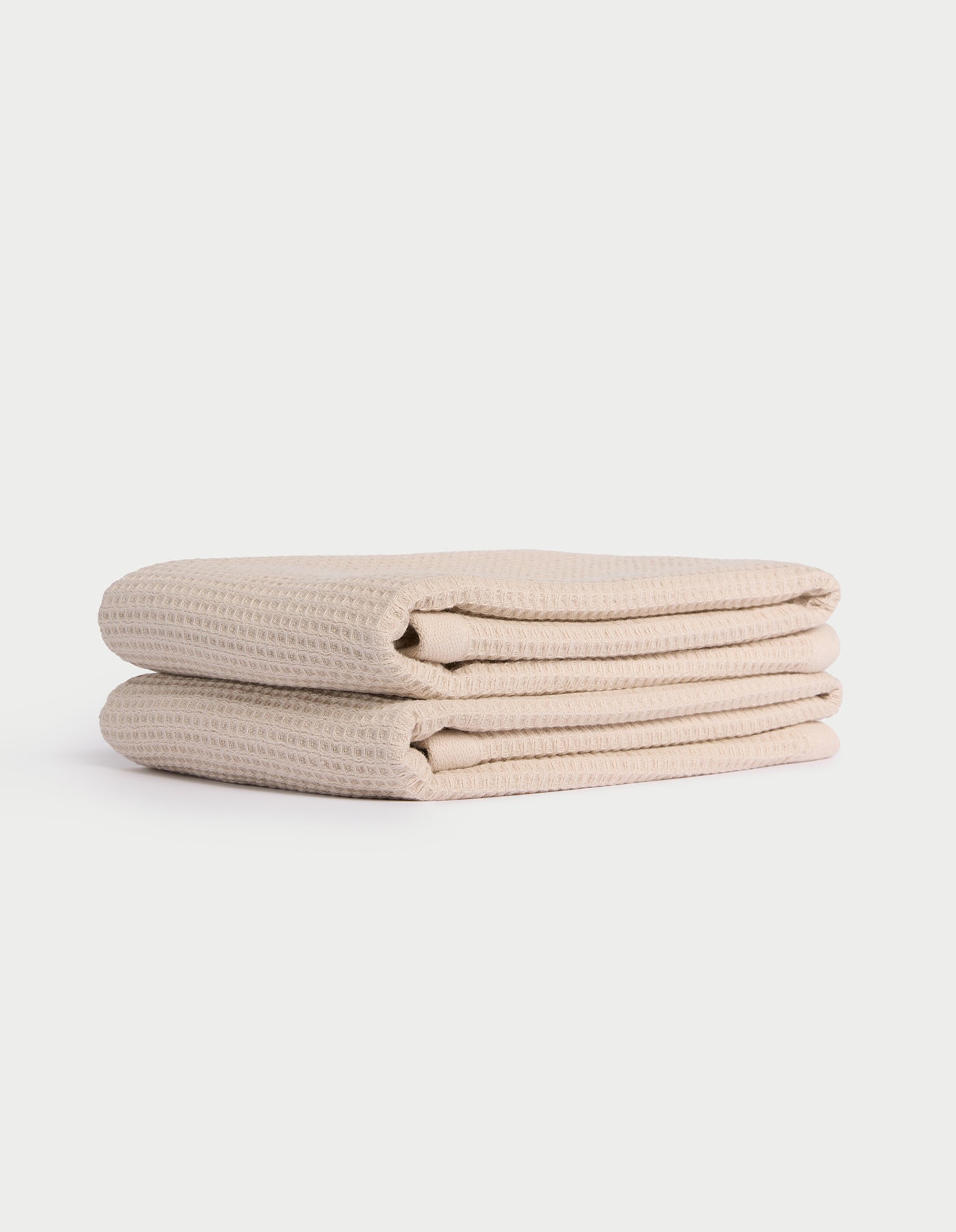 Two neatly folded beige Cozy Earth Waffle Hand Towels stacked atop each other against a plain white background. |Color:Birch