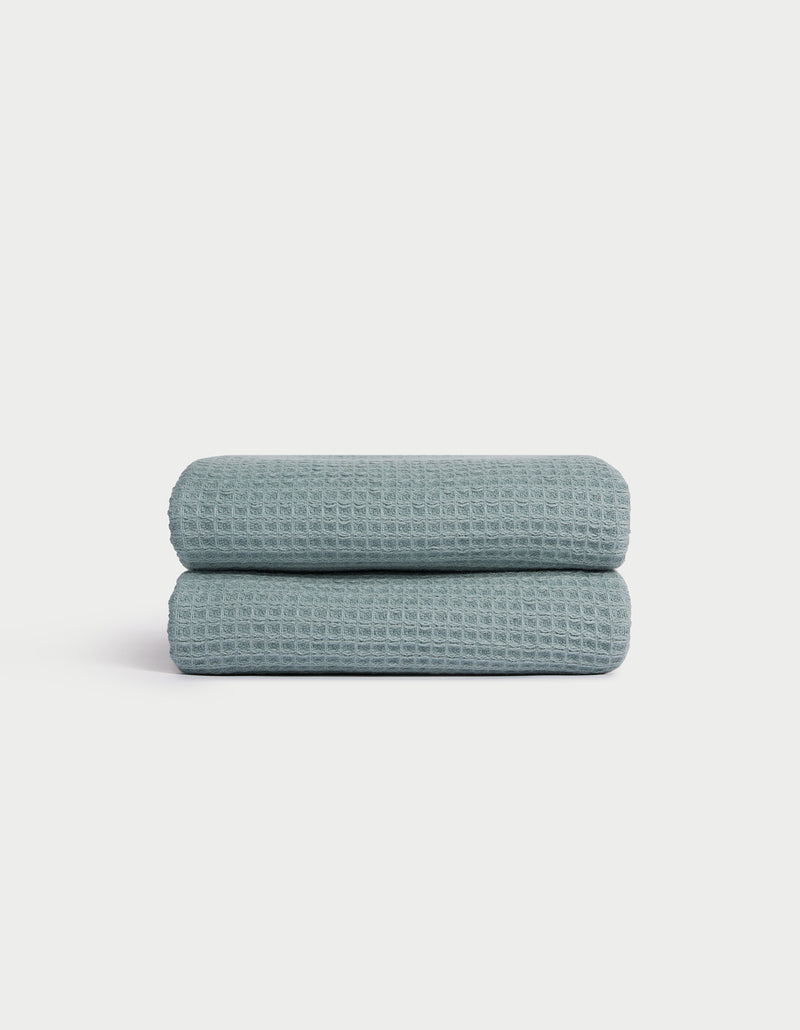 A folded Cozy Earth Waffle Hand Towel in light blue with a textured waffle pattern is displayed on a white background.