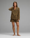 A woman with straight brown hair and a neutral expression stands barefoot against a gray background wearing the Cozy Earth Women’s Bamboo Stretch-Knit Long Sleeve & Short Pajama Set in Leopard Print in Onyx.