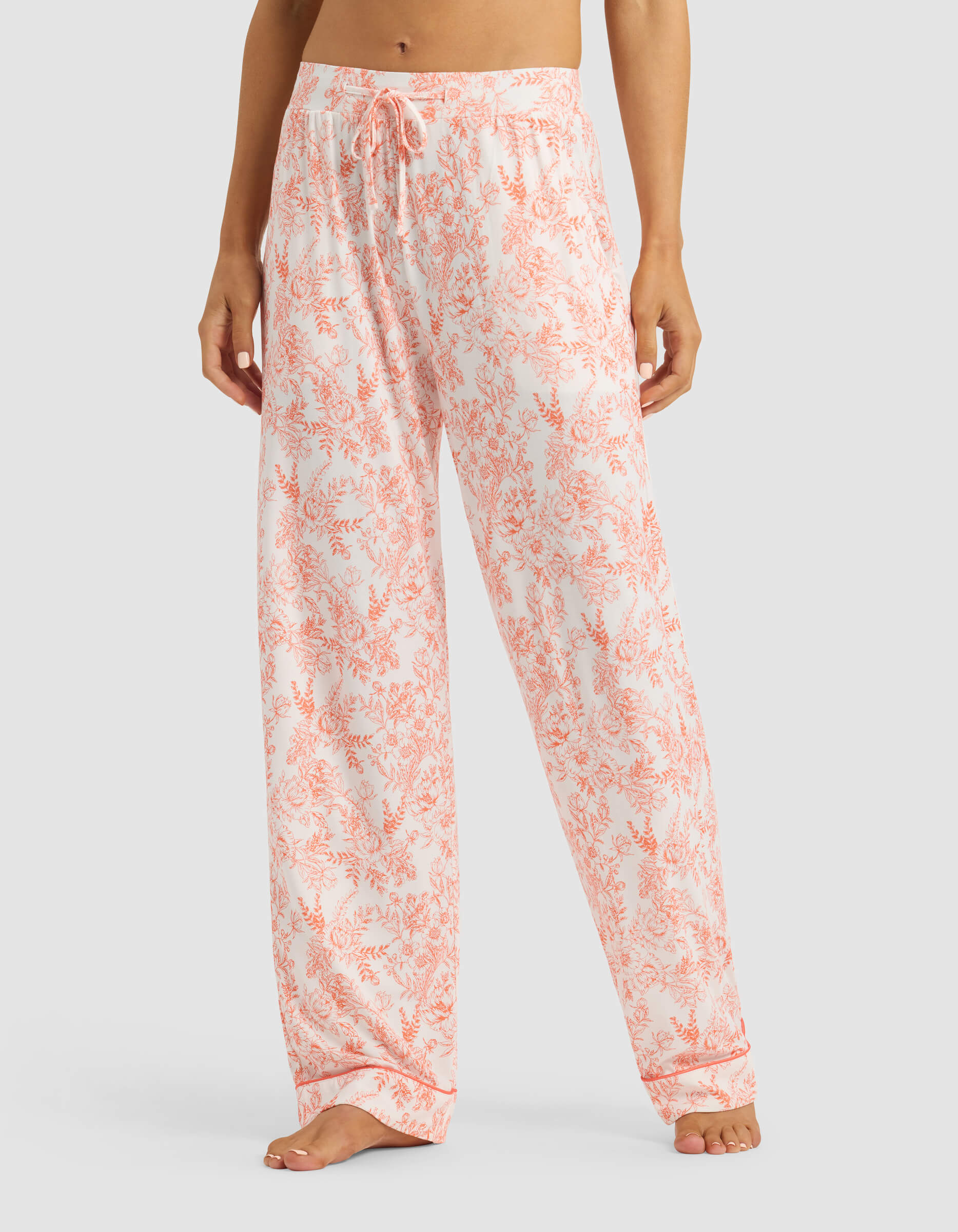 A person models the lower torso and legs wearing Cozy Earth's Women's Bamboo Stretch-Knit Long Sleeve Pajama Set in a light pink and white floral print, standing barefoot against a plain background.|Color:Melon Toile