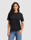 A woman with long dark hair wears the Cozy Earth Women's All Day Tee in black and blue jeans, standing against a light gray background. She faces forward with one hand in her pocket and a neutral expression. |Color:Jet Black